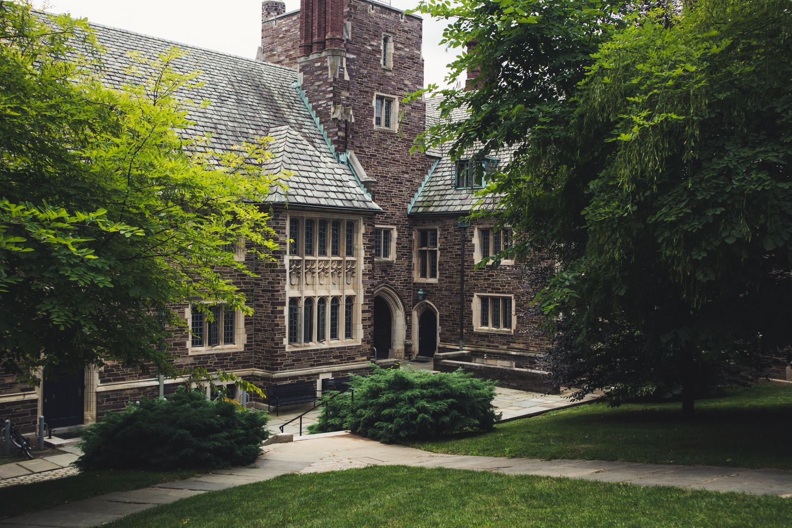 Historic collegiate Gothic stone building framed by trees on a manicured campus